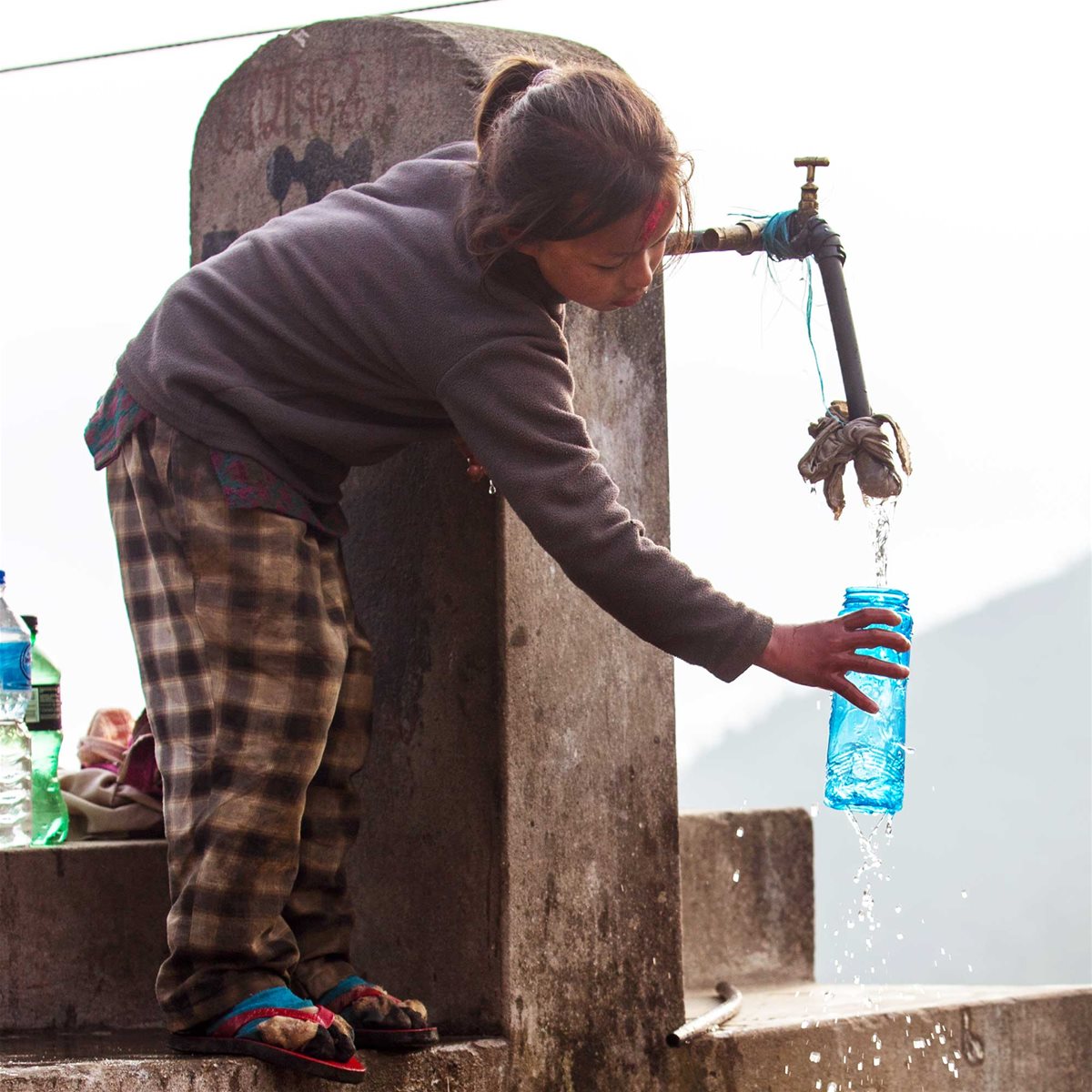 Jente fra Nepal fyllervannflaske fra vannpumpe.